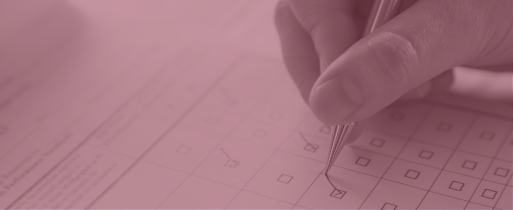 A hand holding a pen checks a box on a paper survey.